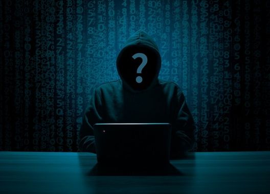 Uma fotografia de um hacker com moletom, capuz sobre a cabeça a frente do notebook e o rosto escuro com um sinal de interrogação