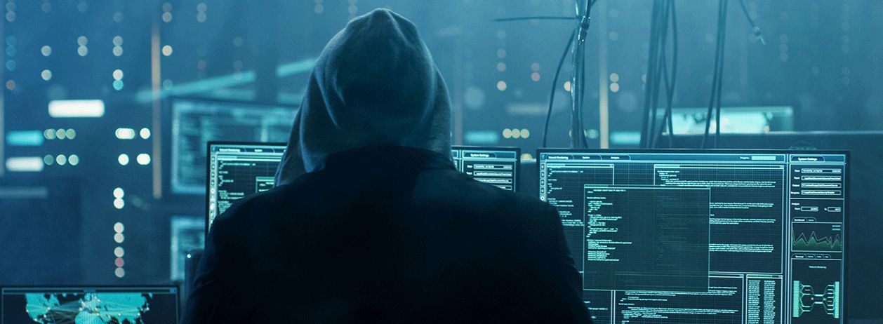 uma foto de uma hacker emcapuzado olhando computadores sincronizados em um ataque hacker