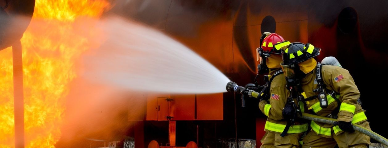 Uma fotografia de bombeiros segurando uma mangueira jogando água contra incêndio