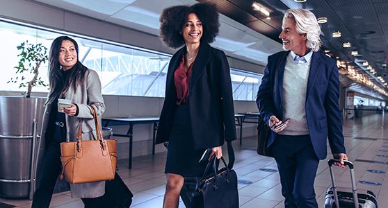 Uma fotografia mostrando duas mulheres e um homemcom malas no saguão do aeroporto para uma viagem corporativa