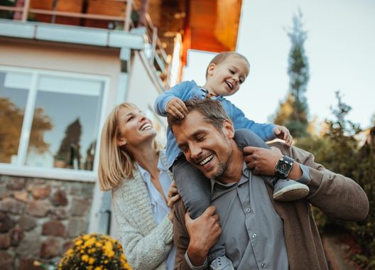 Família feliz, um pai com seu filhinho nos ommbros e a mãe apoiada no braço do pai sorrindo