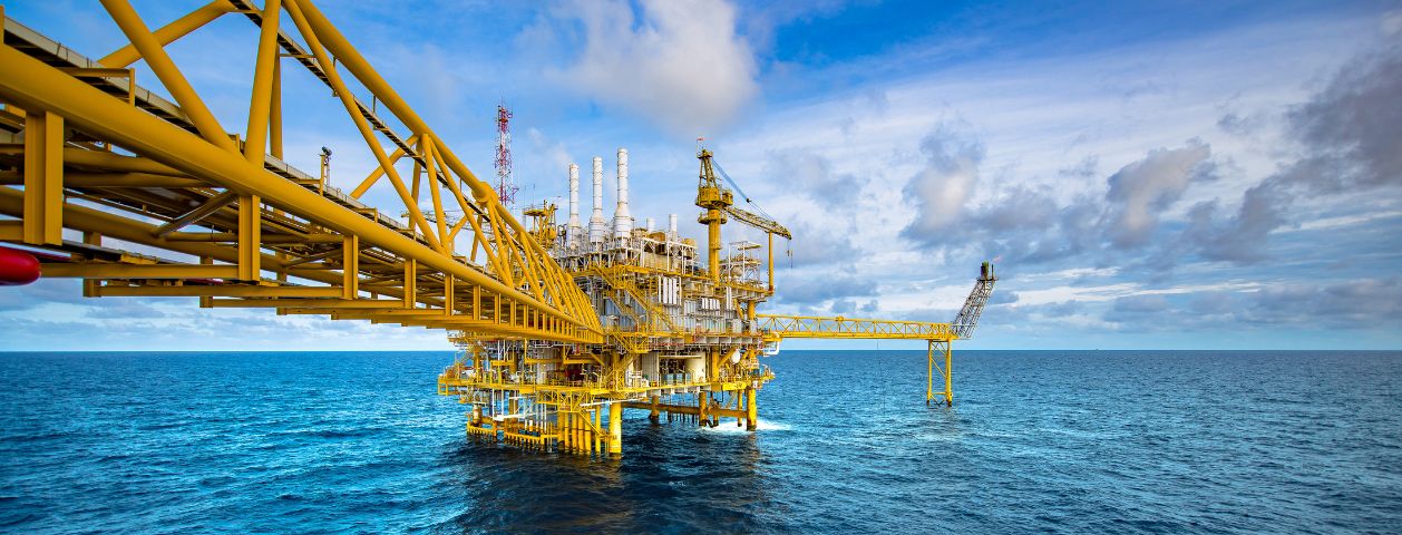 Fotografia de Uma plataforma amarela de petróleo e gás anexada à ponte no meio do mar calmo com céu azul, representando uma empresa offshore