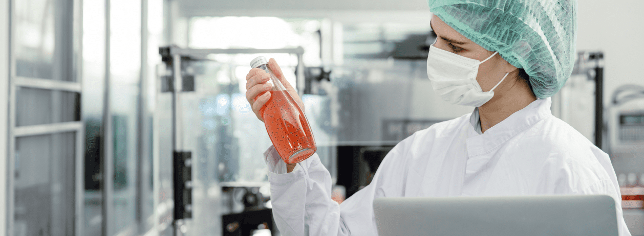 Fotografia de uma agente sanitário de máscara e luva segurando um frasco de algum produto para examinar se está contaminado.