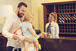 família tocando campainha de recepção em hotel com atendente atrás de balcão sorrindo