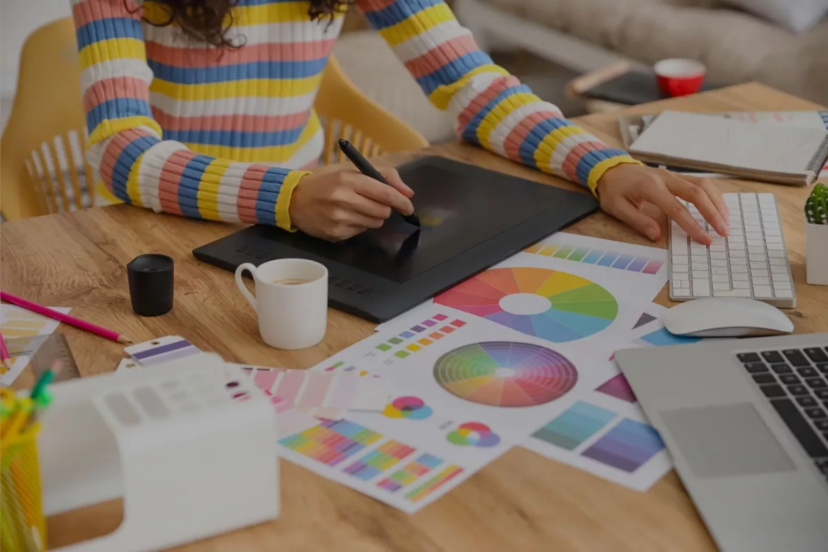 designer com materias comuns em agências de publicidade como gráficos e paletas de cores, mesa digitalizadora e computadores