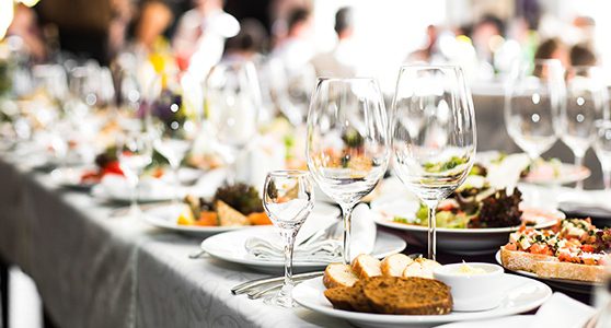 Uma fotografia de uma mesa com um banquete de comidas entre pratos e taças de vidro.