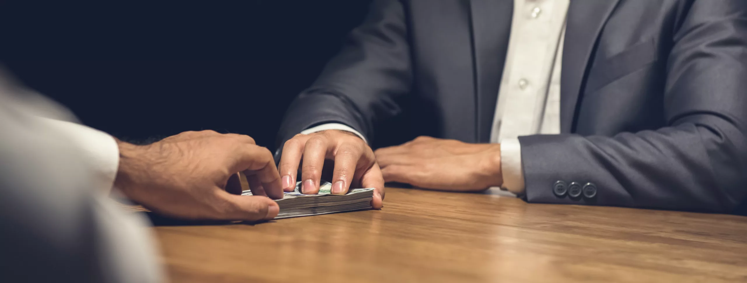 dois homens de terno passando notas de dinheiro em uma mesa representando possível calote financeiro