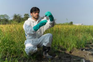 homem com traje de proteção e luvas de borracha analisando substância do solo referente a mitigação de risco ambiental