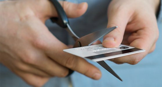 Uma fotografia de pessoa cortando um cartão de crédito com uma tesoura