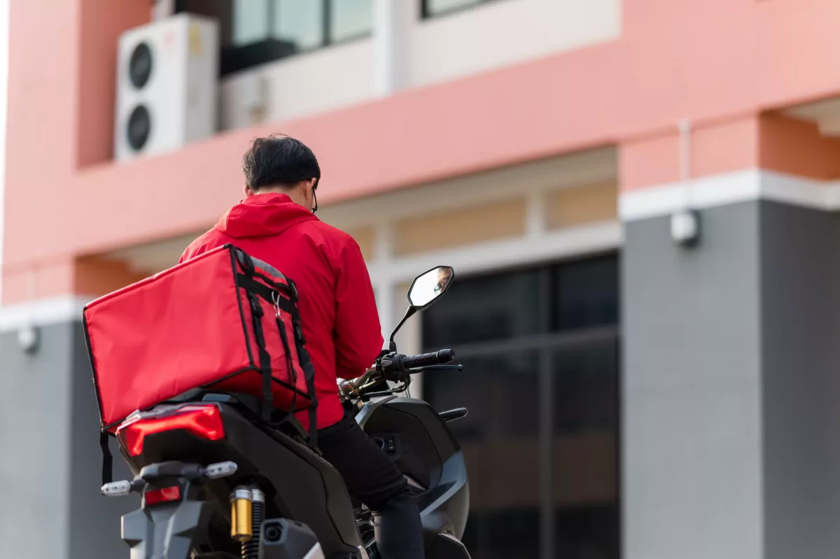 entregador de delivery em moto na frente de prédio, exemplo de economia compartilhada