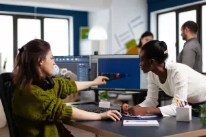 duas mulheres discutindo em mesa de escritório a frente de um monitor