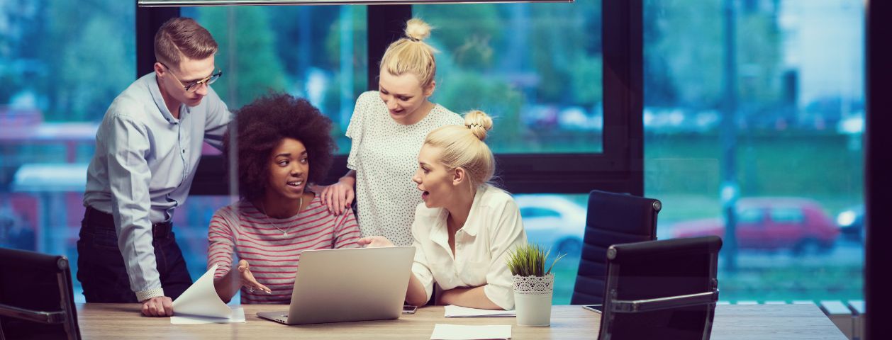 Uma fotografia de um homem e uma mulher em pé apoiando o braço no ombro de duas mulheres sentadas, funcionários discutindo o gerenciamento de riscos em uma startup