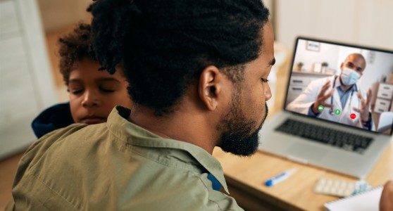 uma fotografia de um homem com o filho no colo em uma consulta online relacionada a importância da contratação para seguro acidentes pessoais, de saúde e de vida.