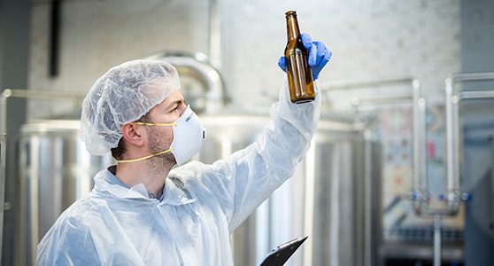 Uma fotografia de um homem segurando uma garrafa na fabrica prevenindo a contaminação de alimentos