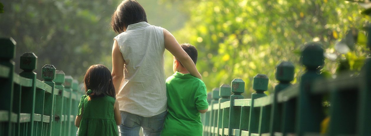 Uma fotografia de mãe com um filho e uma filha pequenos passando por uma ponte verde de madeira