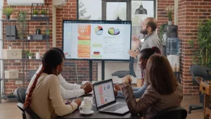 membros de empresa de pequeno porte em apresentação de dados com três pessoas sentadas e uma pessoa de pé apresentando