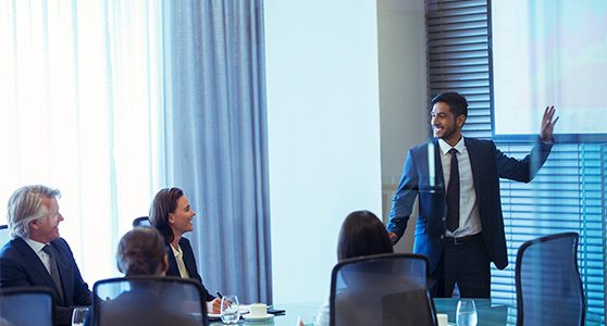 Homem apresentando algo no telão para equipe em reunião