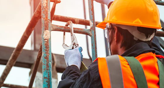 Fotografia mostrando um funcionário de obra subindo uma escada e prendendo o sinto de segurança em uma estrutura de ferro
