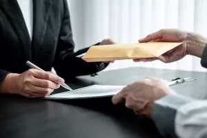 Dois profissionais realizando uma troca confidencial de documentos em um envelope marrom sobre a mesa durante uma negociação.