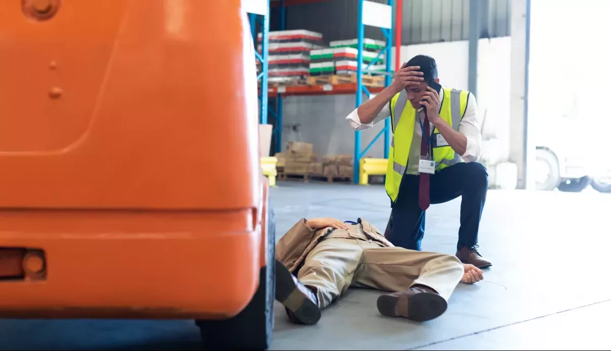 Funcionário de fábrica em pânico com colega de uniforme de fábrica caído ilustrando a importância do Seguro de Acidentes Pessoais