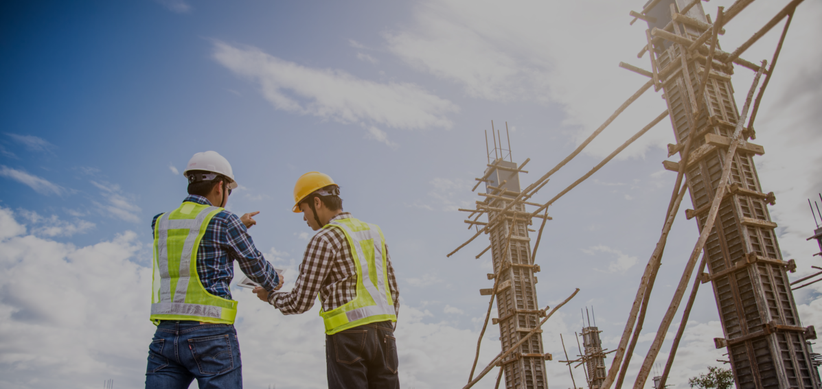 Dois engenheiros com colete e capacete de construção civil ao lado de construção civil em andamento