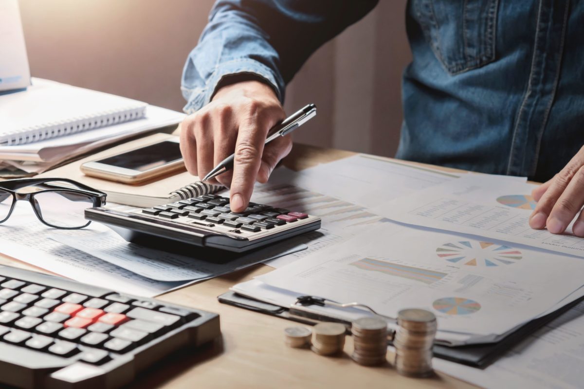 Pessoa operando calculadora em mesa com folhas e teclado representando contenção de riscos com seguro linhas financeiras.