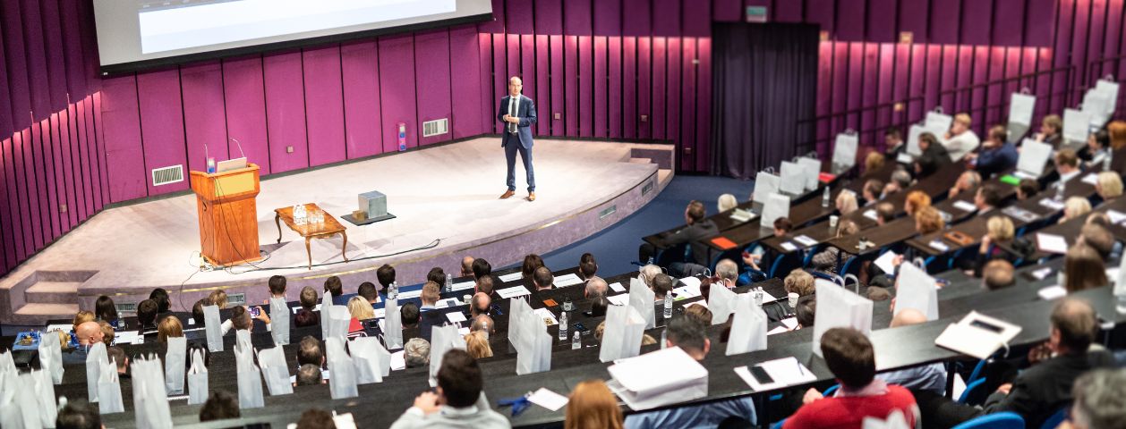 Uma fotografia de um evento com palestrante no palco e o auditório assistindo a evento corporativo coberto por seguro para eventos.