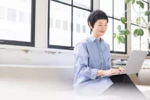 mulher sentada em sofá sorrindo enquanto tecla em notebook