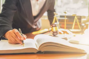 Imagem de advogado assinando livro com martelo e balança da justiça em segundo plano