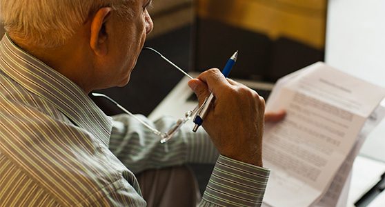 Uma fotografia mostrando um senhor sentado com uma mão segurando o óculos e com a outra segurando um papel de sua indenização de seguro