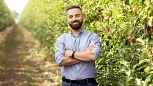 agricultor com camisa azul de braços cruzados na frente de plantação