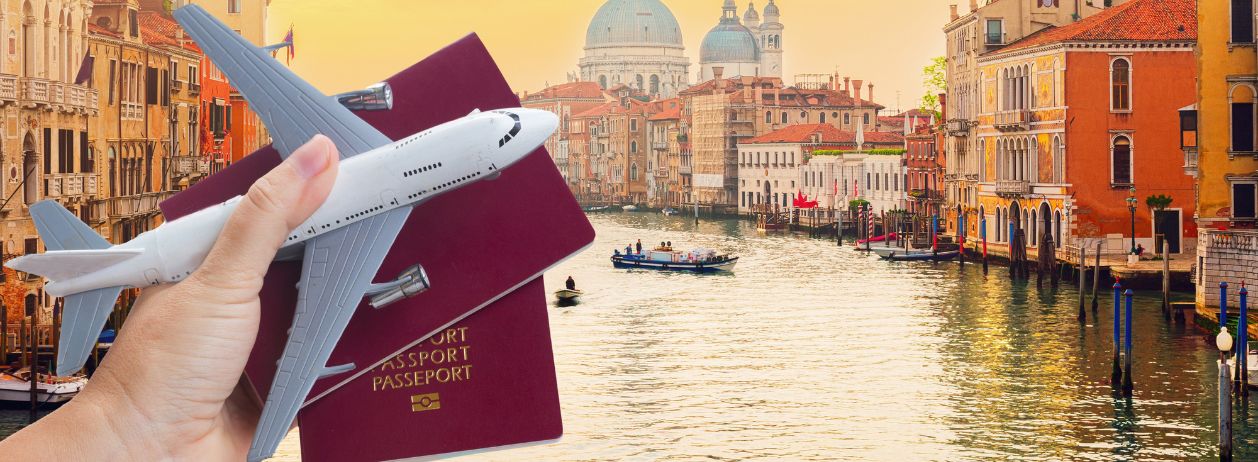 Uma fotografia mostrando uma mão segurando 2 passaportes com uma miniatura de um avião e uma cidade turística ao fundo